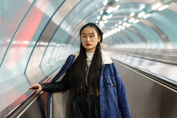 Elegante chica china en traje de moda callejera de moda, abrigo vaqueros, boina de cuero en escaleras mecánicas del metro — Foto de Stock