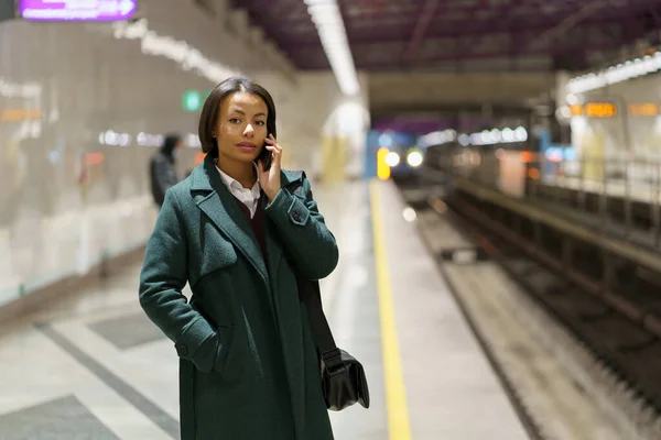 Una seria empresaria africana habla por teléfono en la plataforma del metro mientras espera el tren del metro — Foto de Stock