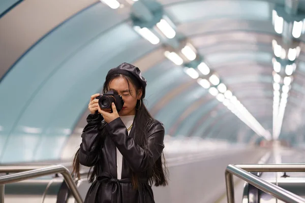 Joven chica coreana elegante hacer fotos en la cámara en el transporte urbano montando escaleras mecánicas mientras viaja — Foto de Stock