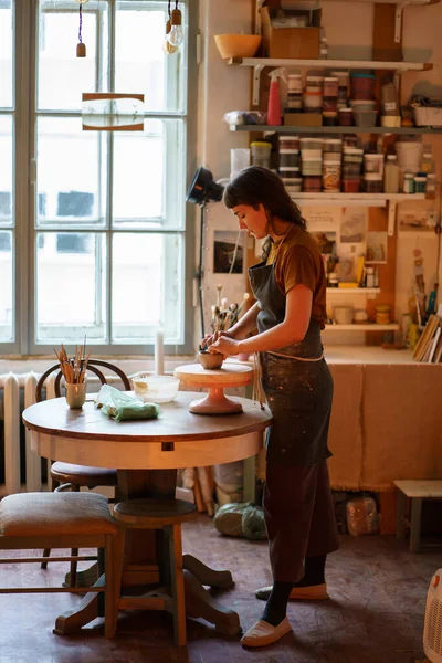 Jeune femme potier travailler avec de l'argile sur la roue de poterie dans l'espace créatif ou studio professionnel — Photo