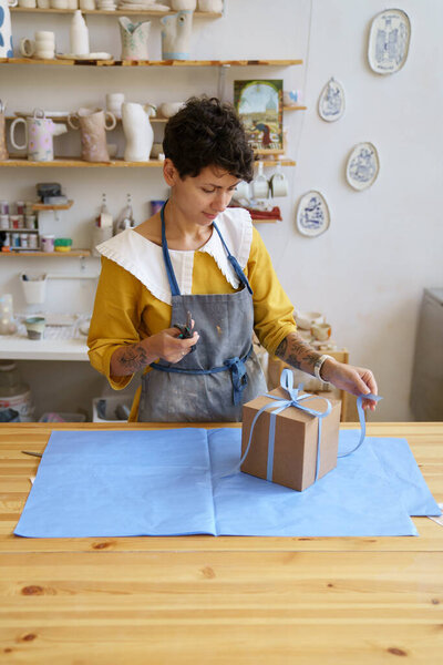 Woman ceramics studio owner packing pottery in gift box for friend birthday or delivery to customer