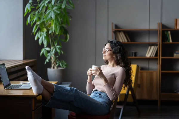 Mulher relaxar em casa acolhedor escritório local de trabalho com os pés descalços na mesa beber chá ou café feliz satisfeito — Fotografia de Stock