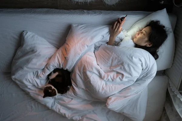 Απάθεια στη ζωή. Νεαρή γυναίκα χωρίς κίνητρα στο κρεβάτι κοιτάζει την οθόνη smartphone, υποφέρει από διαταραχή ύπνου — Φωτογραφία Αρχείου