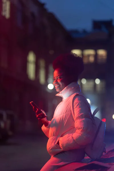 Mladá africká žena v noci s smartphone venkovní čekat na taxi z on-line rezervace aplikace — Stock fotografie