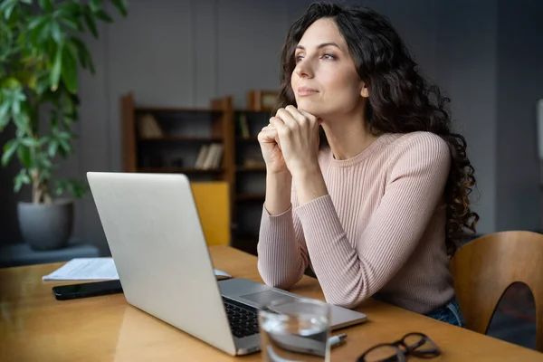 Мрійлива бізнес-леді підприємець дивиться у вікно, віддалене від ноутбука сидить на робочому столі в офісі — стокове фото