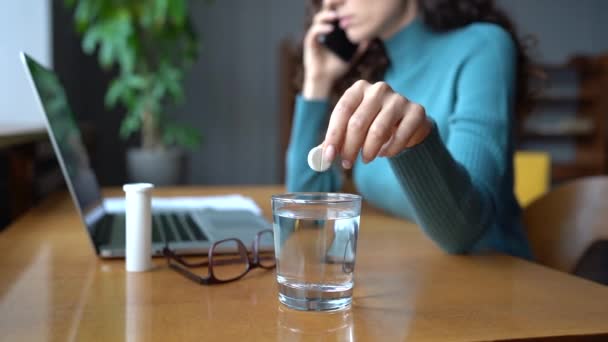 Young business woman dissolves an influenza pill or aspirin in glass of water, talking on phone call — Stock Video