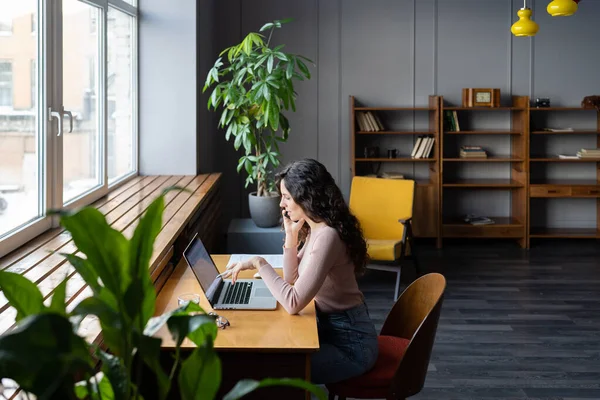 Businesswoman working on laptop in coworking space, discussing financial report via mobile phone — Fotografia de Stock