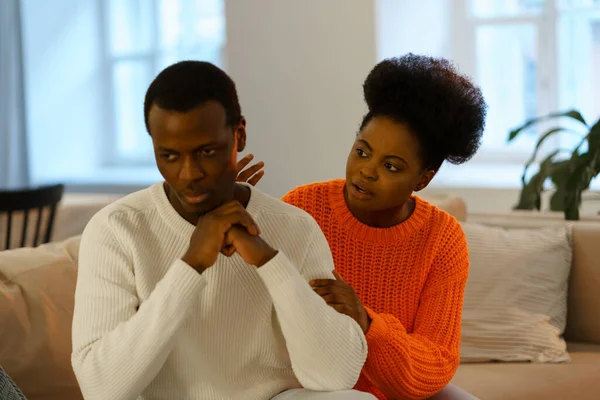 Unhappy african married couple man and woman sitting on couch at home and trying to fix relationship