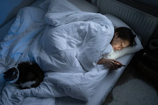 Lonely depressed woman spend night with smartphone sleepless in bed with cat from depression, apathy — стоковое фото