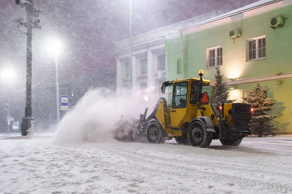 Yellow tractor with rotary sweeper clearing city streets at night in winter. Snow removal equipment — Zdjęcie stockowe
