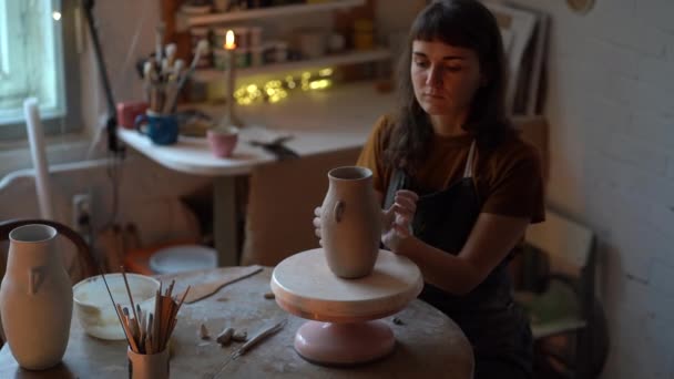 女性は工房や工房で陶器を作る。若い女性は粘土のジャグを形成するアートスペースのテーブルに座る — ストック動画