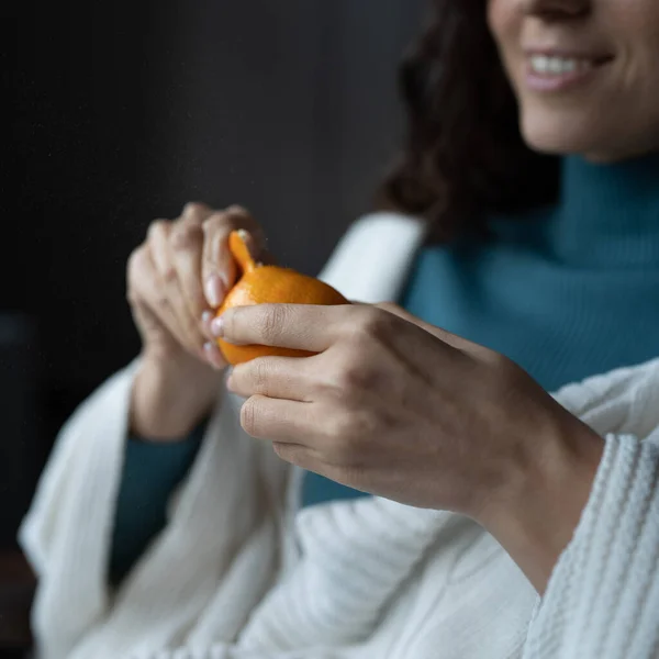 Smiling young woman peels juicy ripe tangerine, home eating seasonal fruits during winter months — Stock fotografie