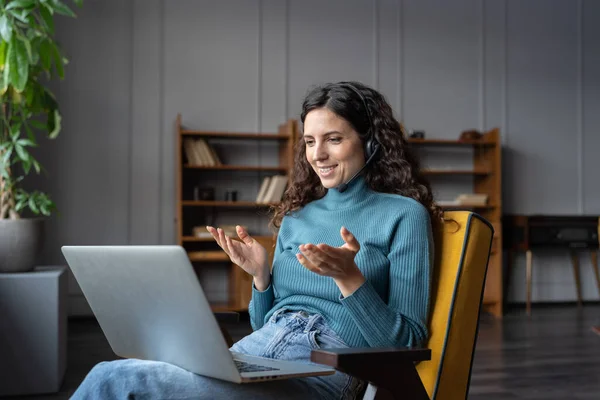 Satisfied female home office employee wearing headset talking online with client via video call — Stockfoto