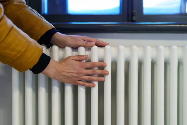 Woman warming hands near heating radiator after winter walk, female checking battery temperature — Stock Photo, Image