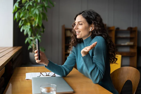 사무실 책상에 앉아서 웃는 여성들은 스마트폰 앱을 통해 온라인으로 전화를 걸어 카메라에 손을 흔들며 이야기를 한다 — 스톡 사진