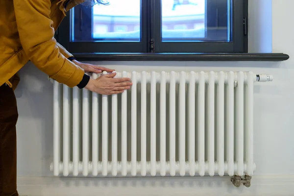 Woman warming hands near heating radiator after winter walk, female checking battery temperature — Stock Photo, Image