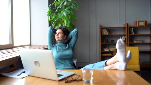 Smiling woman satisfied stretching after laptop work done relax at workplace sit with feet on desk — Stock Video