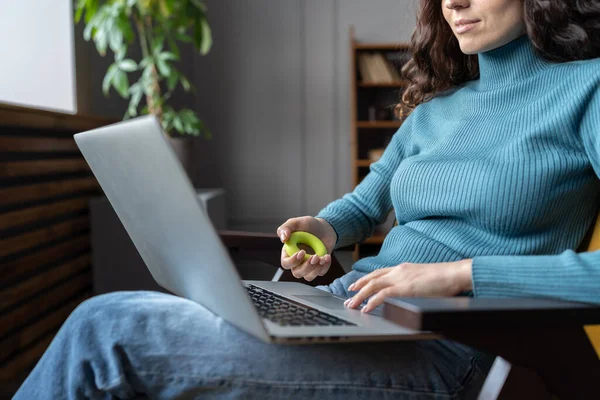 Kobieta pracownik ćwiczenia z ekspanderem ręki podczas pracy na laptopie w biurze — Zdjęcie stockowe