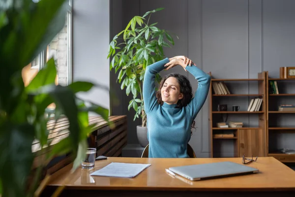 Smiling young female employee relaxing at workplace, stretching and doing gymnastic in office