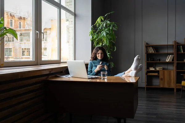 Mulher texto no smartphone, rolar as mídias sociais no local de trabalho relaxado procrastinar com os pés na mesa — Fotografia de Stock
