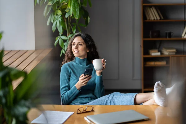 Kvinna sociala medier manager arbete hemifrån sitta vid stängd laptop, fötter på skrivbord dricka morgon kaffe — Stockfoto