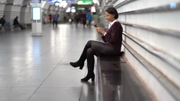 Αφρικανική επιχειρηματίας κάθονται στο μετρό υπόγειο σταθμό πλατφόρμα περιμένετε για τρένο χρησιμοποιώντας smartphone — Αρχείο Βίντεο