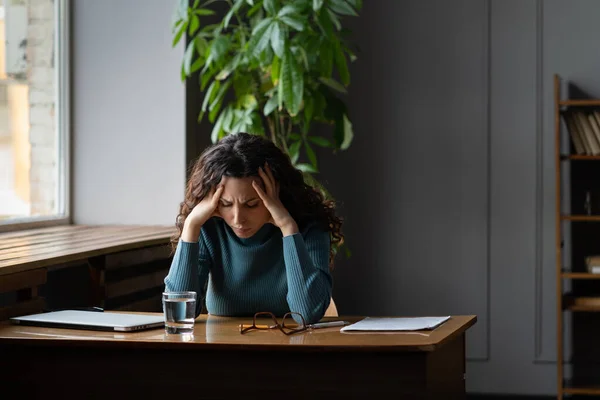 Uitgeputte vrouw zit aan bureau met gesloten laptop moe van overwerk, burn-out en gebrek aan inspiratie — Stockfoto