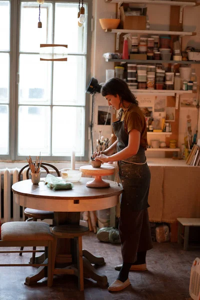 Jeune femme potier travailler avec de l'argile sur la roue de poterie dans l'espace créatif ou studio professionnel — Photo