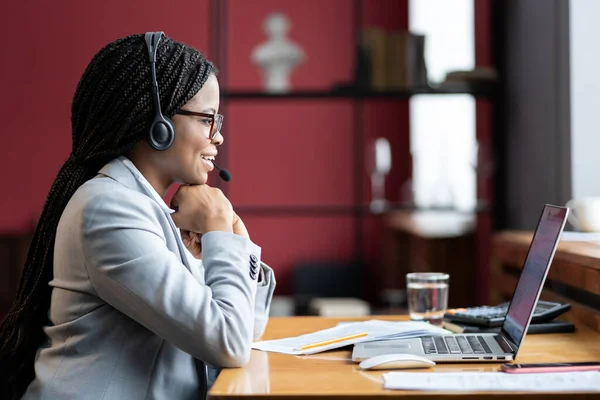 Joven sonriente mujer africana madre en licencia de maternidad en auriculares inalámbricos trabajando remotamente desde casa — Foto de Stock