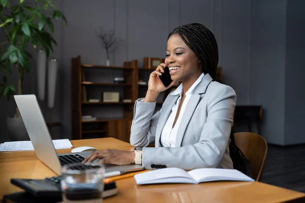快乐的非洲女商人坐在办公室打电话给朋友、家人或满意的客户 — 图库照片