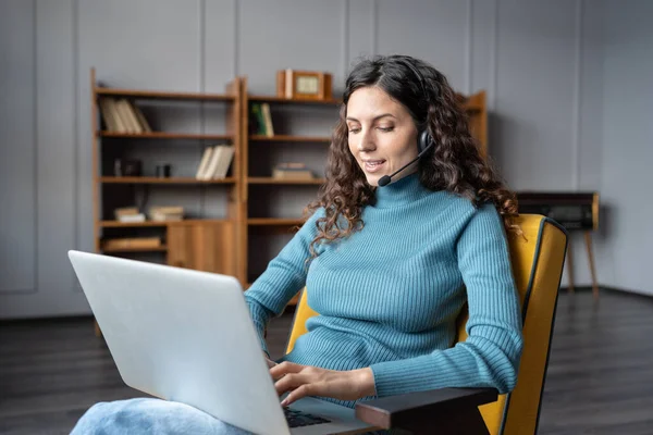 Giovane donna piacevole in cuffia utilizzando computer portatile parlando con il partner tramite video chat da casa — Foto Stock