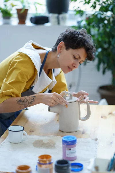 Jeune femme en tablier apprenant à faire de la céramique pendant la masterclass en atelier de poterie — Photo