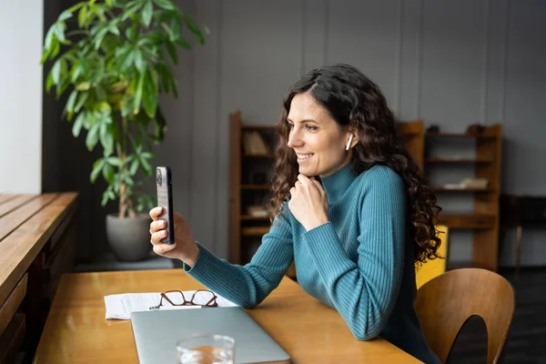 무선 이어폰을 사용하여 직장에서 비디오 통화를 하는 젊은 여성 직원들에게 행복하게 미소짓고 있다 — 스톡 사진
