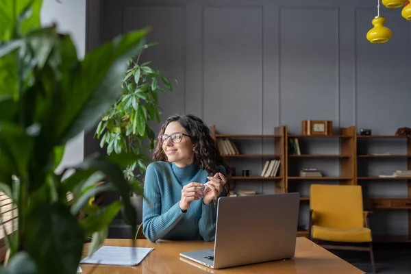 Glad nöjd kvinnlig anställd tittar i fönstret medan du tar paus från datorarbete — Stockfoto