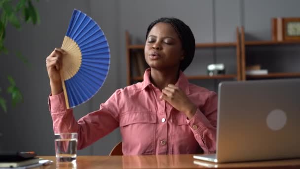 Travailleuse africaine en sueur assis à l'ordinateur portable au bureau chaud essayer d'éviter la surchauffe en utilisant un ventilateur de papier — Video