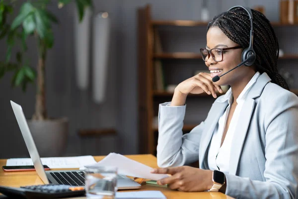 Young positive afro female using wireless headset for remote work during maternity leave