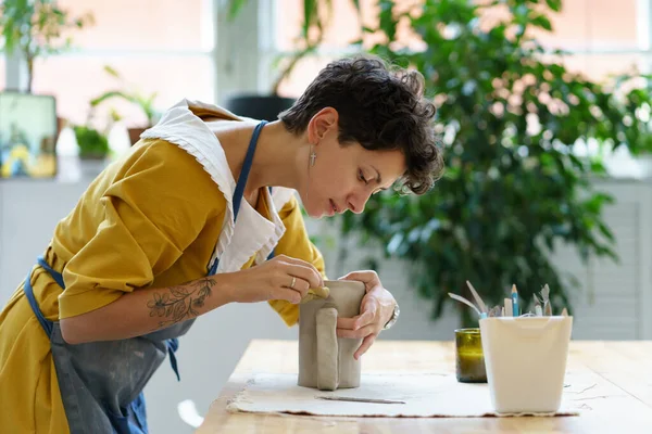 Молода дівчина-художниця зайнята моделлю глечика з сирої глини під час уроку кераміки або майстерні в студії — стокове фото