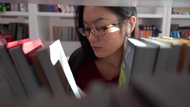 Estudante chinês feminino procura livro na biblioteca em busca de material para pesquisa de trabalho universitário — Vídeo de Stock