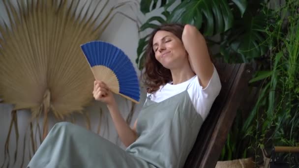 Mladá uvolněná zasněná žena pomocí papírového ventilátoru při relaxaci v krásné osvěžující domácí zahradě — Stock video