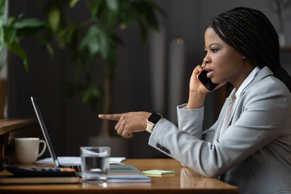 Choqué malheureux afro femme d'affaires parler au téléphone doigt de pointage à l'écran de l'ordinateur portable résoudre problème — Photo
