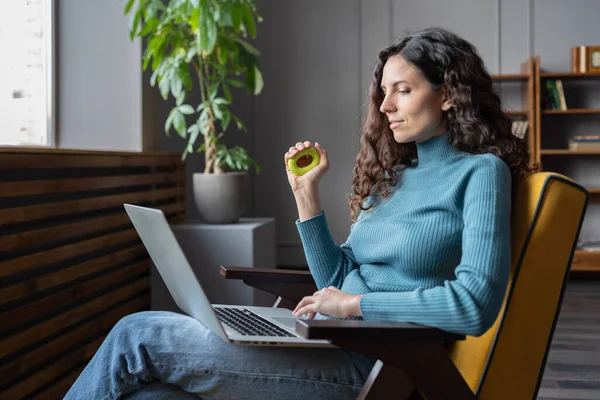 Młody zadowolony kobieta pracownik ściskając nadgarstek ekspander w rękę i patrząc na laptop ekran — Zdjęcie stockowe