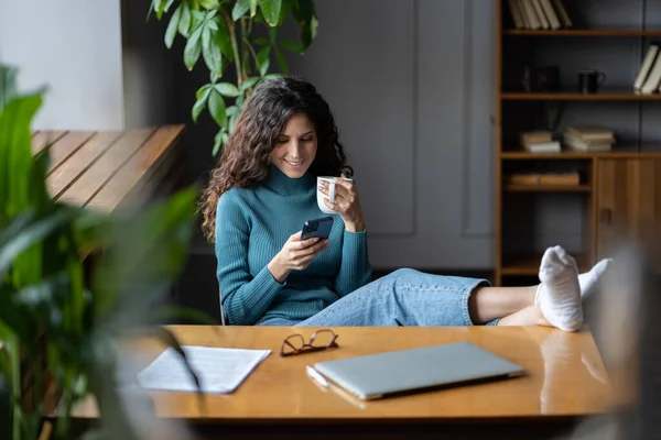 Onderbreking tijdens de werkdag. Vrouwelijke werknemer rust na het werk, het drinken van koffie en het gebruik van de smartphone — Stockfoto