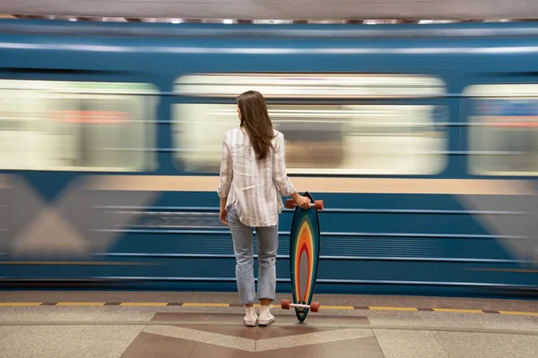 Chica esperar a que el metro de coches en la estación con el tren que pasa en segundo plano. Vista trasera de la mujer en la plataforma — Foto de Stock