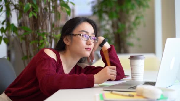 Cansado entediado asiático estudante menina em fones de ouvido surf internet no laptop enquanto estuda na biblioteca — Vídeo de Stock