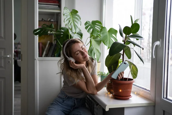 Sourire femme rêvant, écouter de la musique porter des écouteurs sans fil en utilisant un téléphone mobile à la maison — Photo