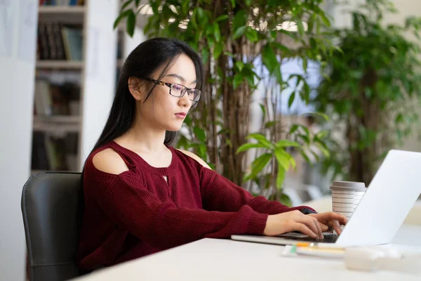 진지 한 여학생 이 대학 도서관에서 원격 교육을 위해 노트북 컴퓨터를 사용 한다. — 스톡 사진