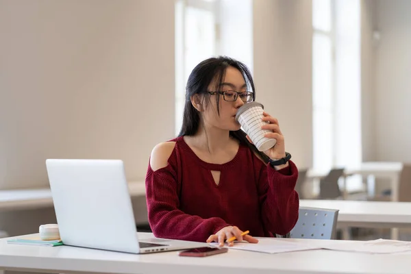 Asiatisk kvinnlig student dricker kaffe medan förbereda sig för tentor i bibliotekets läsesal — Stockfoto