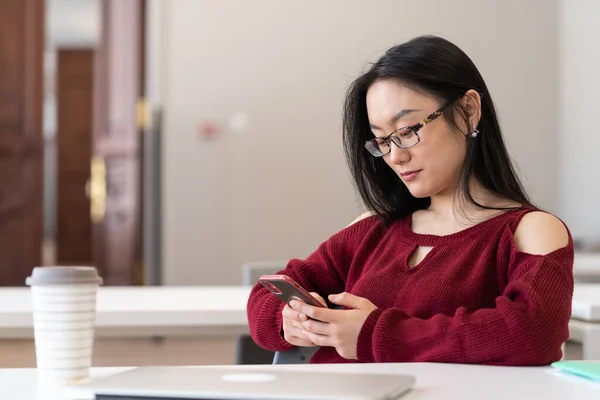 대학 도서관에서 공부하면서 스마트폰으로 소셜 미디어를 통해 수다를 떨고 있는 아시아인 여학생 — 스톡 사진