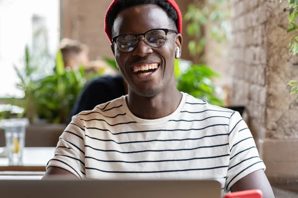 Rire homme afro-américain hipster en utilisant un ordinateur portable, parler en ligne dans le chat vidéo avec des amis dans le café — Photo
