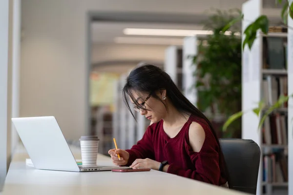 Nördig asiatisk tjej i glasögon som arbetar med universitetets forskningsprojekt i biblioteket — Stockfoto